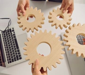 أيدي تمسك تروس خشبية فوق طاولة عمل، رمزًا للتعلم المستمر والابتكار في العمل الخيري 