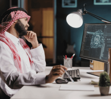 رجل سعودي يرتدي شماغًا يعمل على تحليل بيانات على شاشة كمبيوتر لابتكار حلول تنظيمية ذكية في مؤسسة غير ربحية 